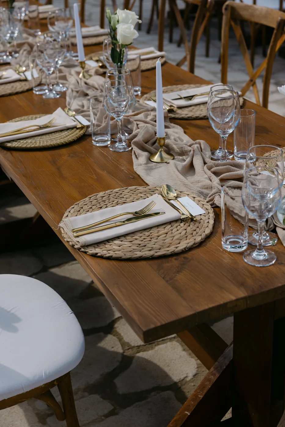 Beaded gold charger, folded neutral napkin, cutlery and delicate glassware on a wooden reception table.